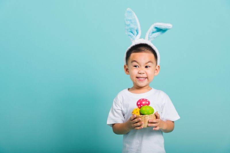 child with bunny ears and an easter basket with choc eggs