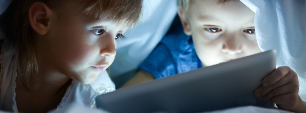 children reading an iPad under the covers