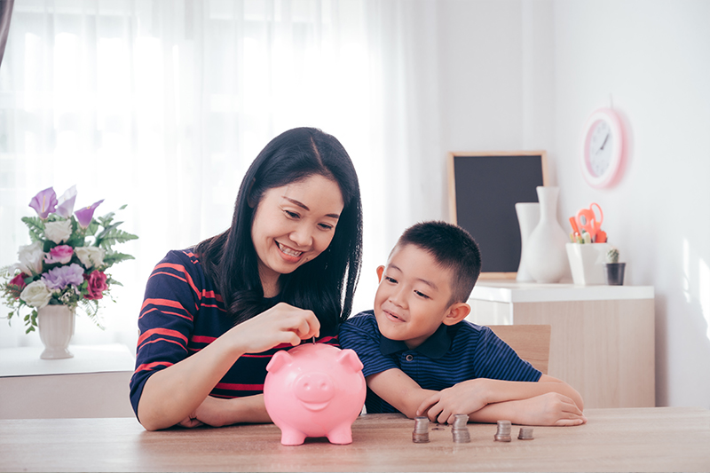 mum putting pocket money into piggy bank with kid sitting next to her