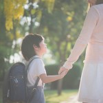Asian,Mother,Holding,Hand,Of,Little,Son,With,Backpack,Outdoors,