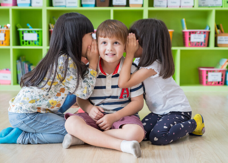 two children whispering in a boy's ear