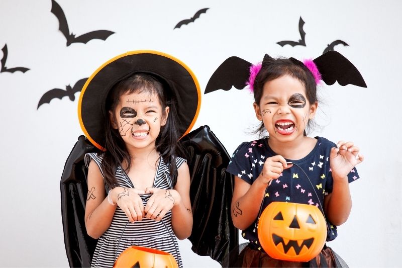 Two little girls dresses in halloween costumes holding pumpkins