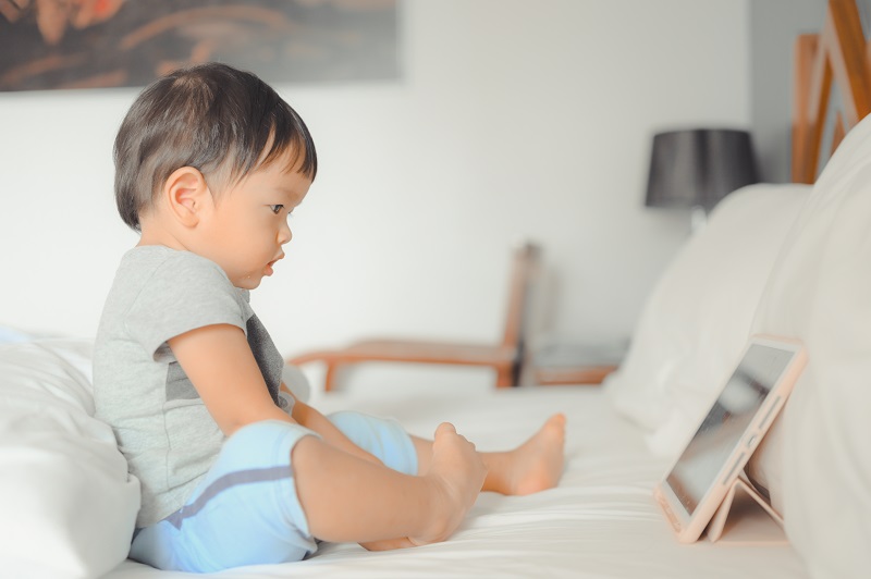 A small boy watching a tablet in bed